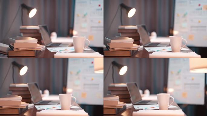 摇臂镜头拍摄的工作桌，桌上满是纸质文件、图表、笔记本电脑和台灯，背景是家中工作室的深夜场景。