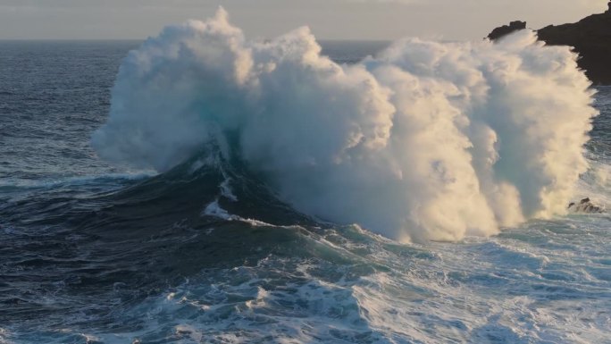 巨大的海浪在日落天空背景下猛烈撞击。慢动作展示了风暴海浪在马德拉岛波尔图莫尼兹海岸的溅起。
