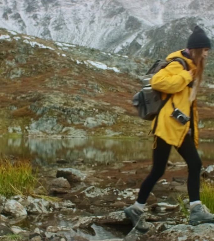 秋天，女性徒步旅行者在山湖附近穿越溪流。