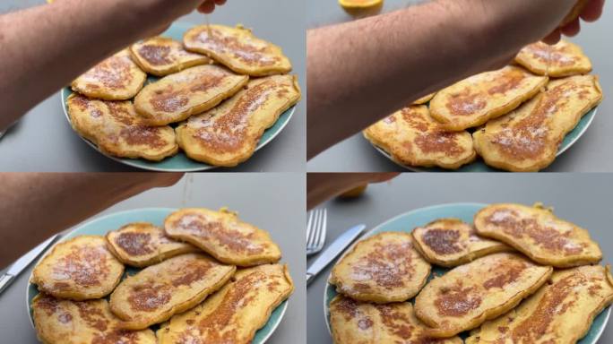 一只手在装满金色煎饼的盘子上挤柠檬，煎饼上轻轻撒上糖，并淋上新鲜橙汁。