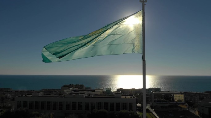 AKTAU, 哈萨克斯坦 - 2025年2月1日：阳光照耀在城市天际线和闪烁的里海上，绿色旗帜在明亮