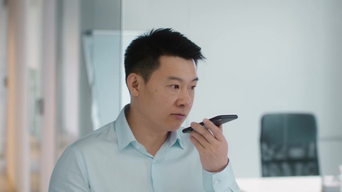 快速现代沟通。成熟的亚洲商人特写肖像，正在智能手机上录制语音信息。