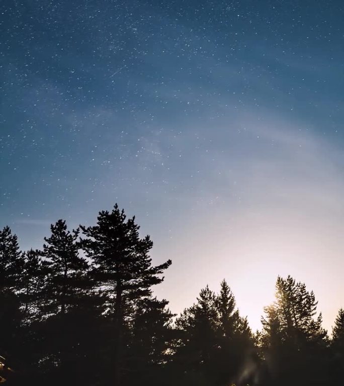 朋友们在星空下的篝火旁坐着，月光照耀下的银河星空，垂直天文延时摄影。