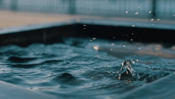 水滴落在光滑的黑色表面上，形成扩散的涟漪和轻柔的溅水，精准的慢动作捕捉液体优雅的运动和冲击。