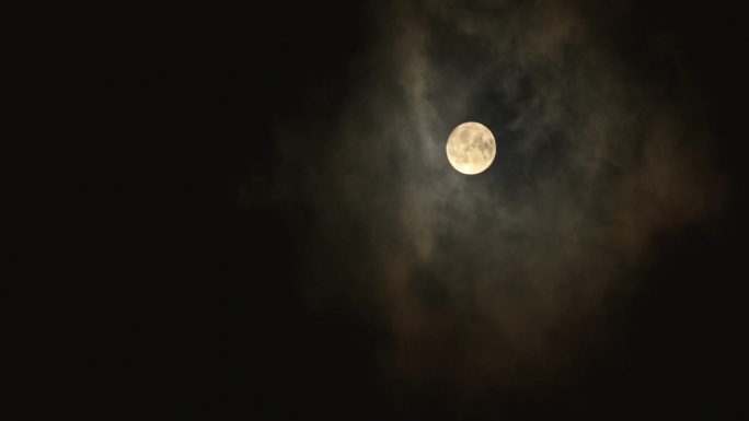 满月在黑暗的夜空中透过云层闪耀。