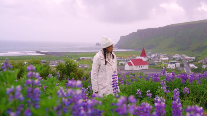 年轻女性在紫花狼毒花田中欢笑，背景是冰岛的一座教堂。
