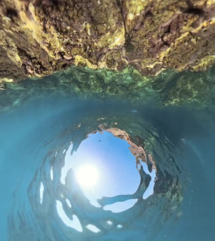 竖屏视频。全景360度球形全景图：一块大型岩石结构沉没在清澈的水下，阳光透过水面洒下，形成岩石边缘柔