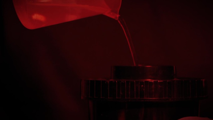 在摄影工作室冲洗照片。老式胶卷底片处理。红光暗房。一个男人正在倒化学药品。