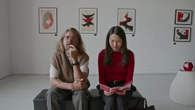 男人和女人坐在软垫上，正在艺术画廊中查看艺术作品和宣传册。
