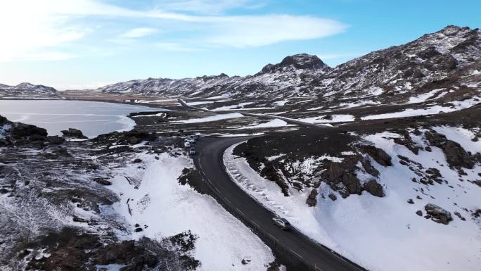 灰色轿车在冰岛雪山公路上行驶，空中推进镜头，白天。