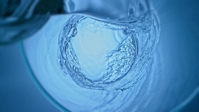 纯净水旋转进入旋转的玻璃杯，形成气泡和漩涡效果。