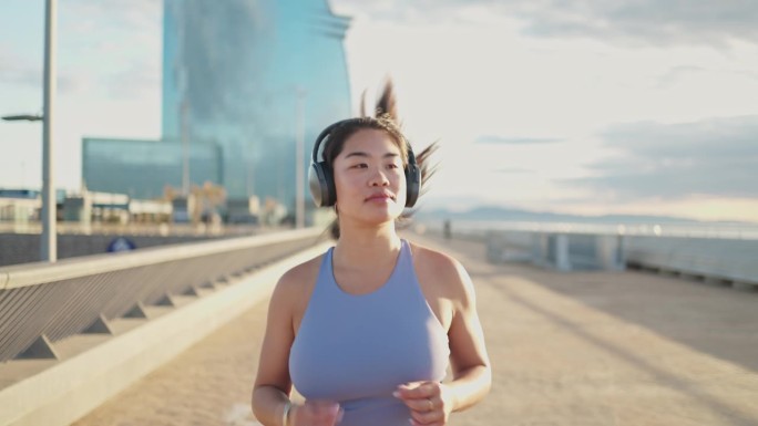 年轻的亚洲女性在城市中慢动作跑步，耳机在耳。