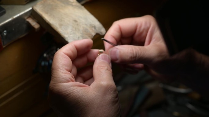 金匠小心翼翼地制作复杂的金色吊坠，专注地锤打精致的细节，展现出精湛的金属加工工艺。