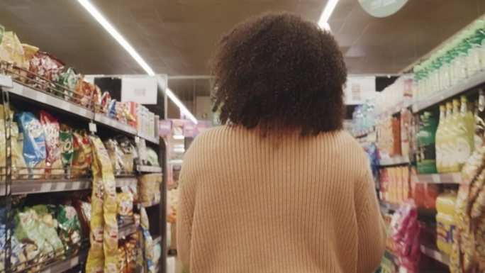 一个留着爆炸头的女人在超市的小岛上走过的背影。年轻女性在当地杂货店购买新鲜农产品和家庭用品
