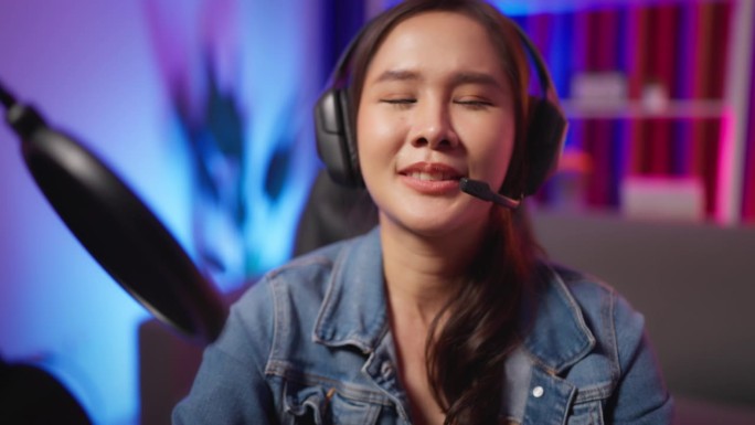特写拍摄年轻迷人的女博主/游戏玩家/Dj/主持人坐在耳机与耳机，看着和说话的相机，与霓虹灯背景直播。