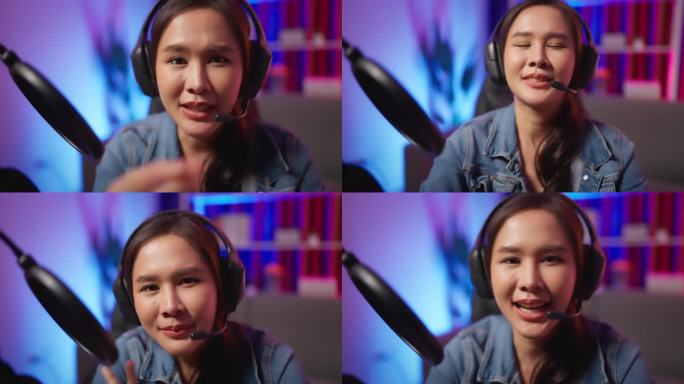 特写拍摄年轻迷人的女博主/游戏玩家/Dj/主持人坐在耳机与耳机，看着和说话的相机，与霓虹灯背景直播。