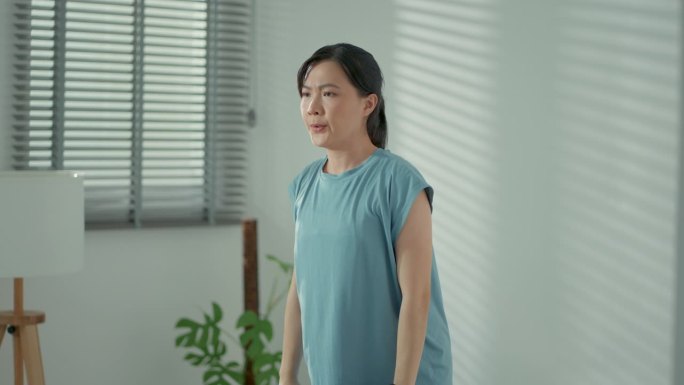 亚洲女性在家里的客厅里用哑铃做运动训练，感到疲惫不堪。