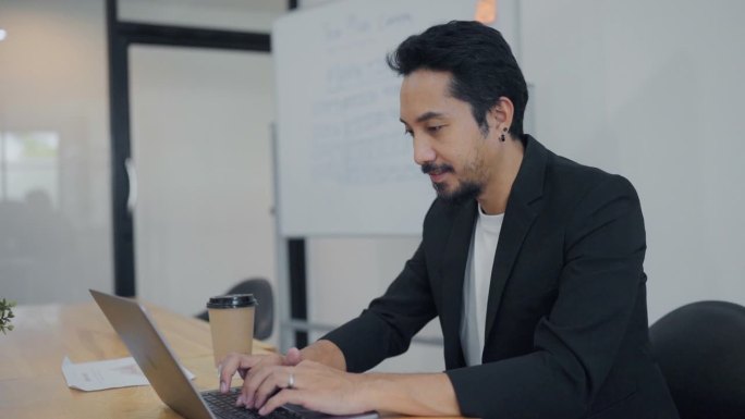 专注于项目的亚洲商人，使用公司的电脑软件，坐在办公桌前。