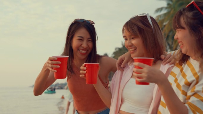一群年轻的亚洲女性在热带海滩上喝酒庆祝。