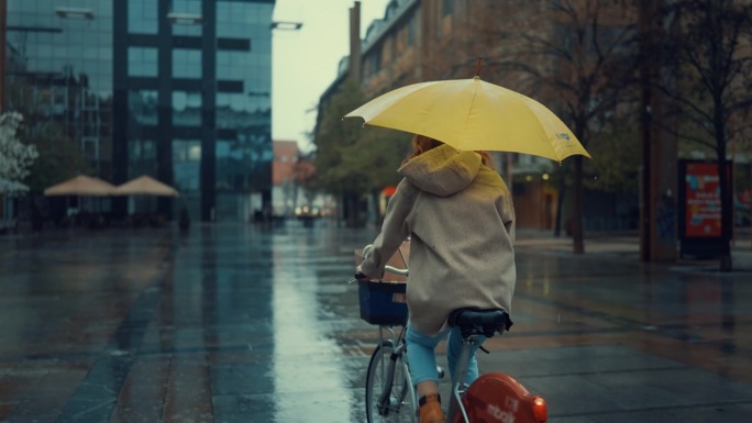 打着黄伞的年轻女子在雨中骑自行车
