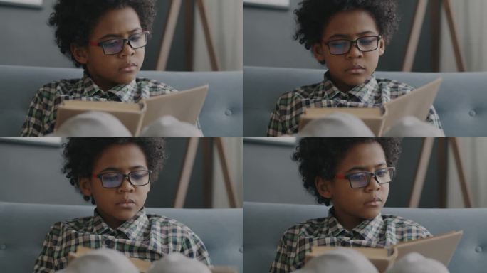 聪明的非裔美国男孩戴着眼镜在家里看书微笑的慢镜头