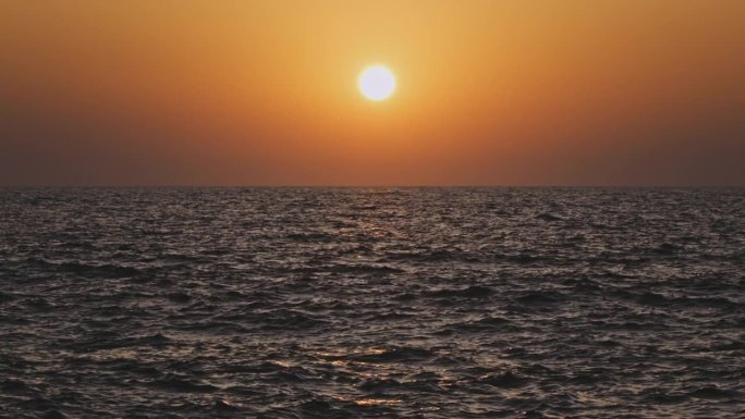 橙色的天空和日落在灰色的大海或海洋的平静波浪上。宁静、禅宗般的电影场景。慢动作视频。