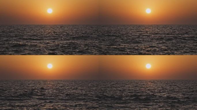 橙色的天空和日落在灰色的大海或海洋的平静波浪上。宁静、禅宗般的电影场景。慢动作视频。