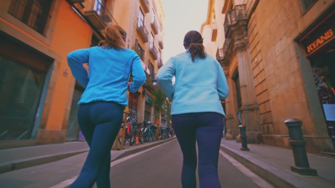 慢镜头的妇女慢跑在街道上的城市。女性朋友在建筑物中奔跑。他们过着积极的生活方式。