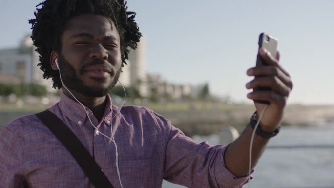年轻的非洲裔美国人在美丽的海边背景下用智能手机视频聊天技术聊天，微笑着享受谈话
