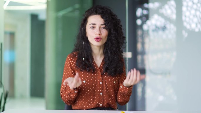 摄像头的观点。一位自信的女商人坐在现代办公室的办公桌前，通过视频连接进行交谈。