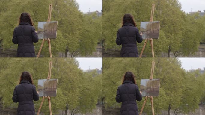 一个女人在塞纳河附近画画。一位富有创造力的女艺术家站在巴黎的画架旁，用画笔作画。女艺术家，艺术销售，