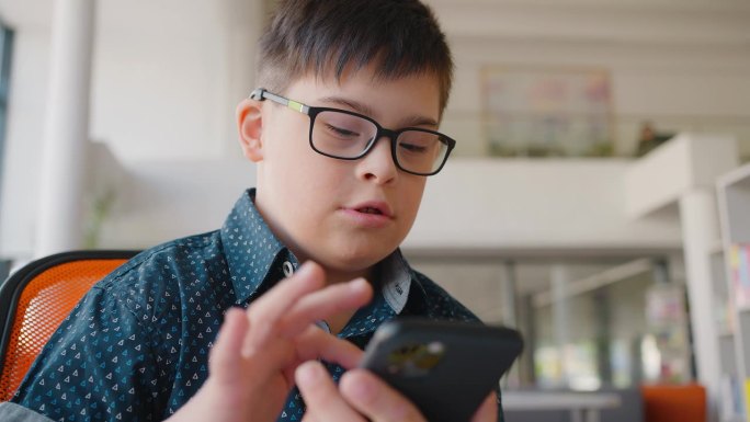 患有唐氏综合症的残疾男孩在玩虚拟网络游戏时使用智能手机的照片