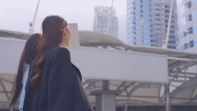 两个亚洲女商人自信地走在城市的户外。迷人美丽的女员工员工人们感到快乐和放松，同时度过闲暇时间走到办公