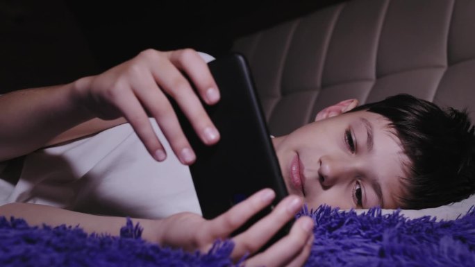 晚上娱乐:男孩躺在床上玩手机