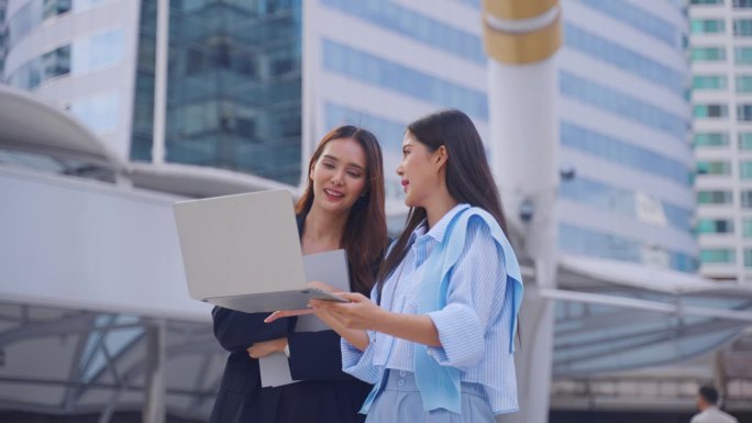 两个亚洲女商人自信地走在城市的户外。迷人美丽的女员工员工人们感到快乐和放松，同时度过闲暇时间走到办公