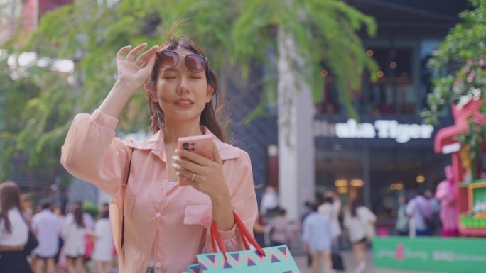 亚洲美女在逛百货商店时看着地图。年轻漂亮的女顾客拿着购物袋，开心地用智能手机在商场中心购物。
