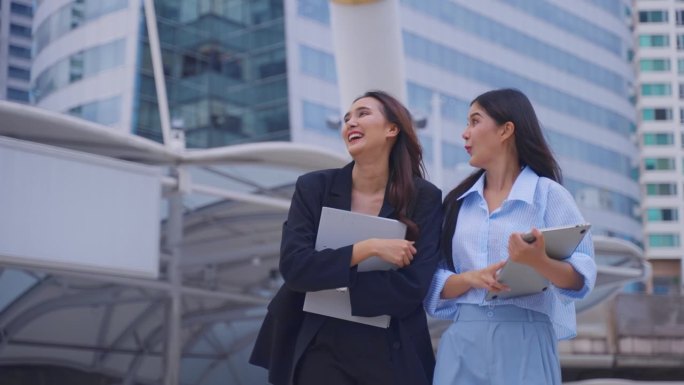 两个亚洲女商人自信地站在城市的户外。迷人美丽的女员工员工人们感到快乐和放松，同时度过闲暇时间走到办公