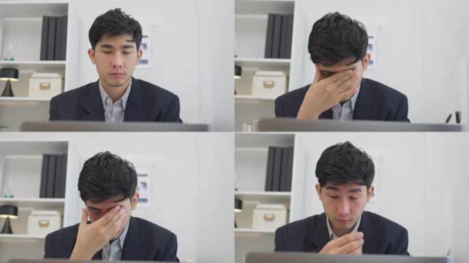 亚洲商人在现代办公室里使用笔记本电脑工作时，穿着西装，疲惫不堪