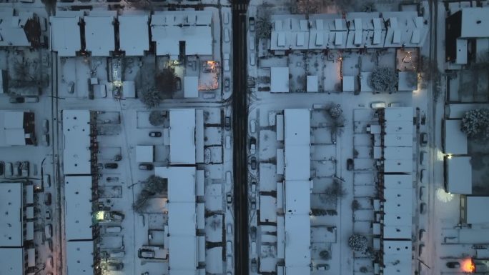 美国城市夜间的街道上有小雪。屋顶上新下的雪。光线反射在潮湿的街道上。卡车航拍。