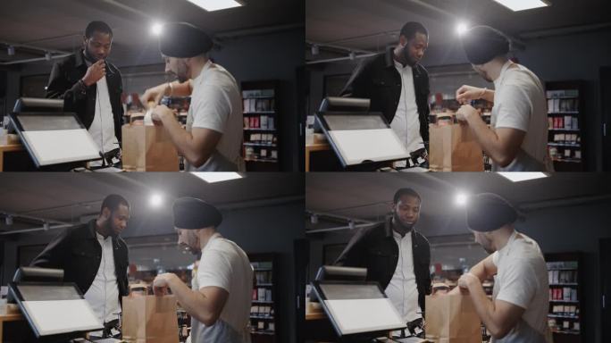 一名印度收银员正在给一名非洲男性顾客打包一袋杂货