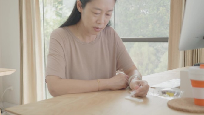 一名患有糖尿病的东南亚妇女在家中使用血糖自测仪检查血糖