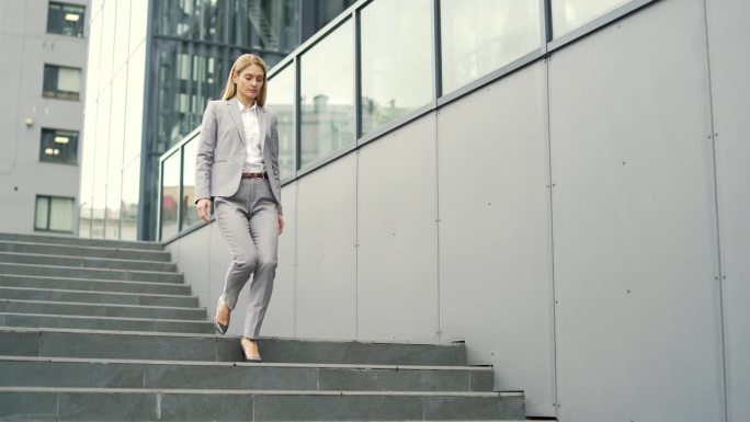 一位穿着正装的自信的女商人走下办公楼前的楼梯。