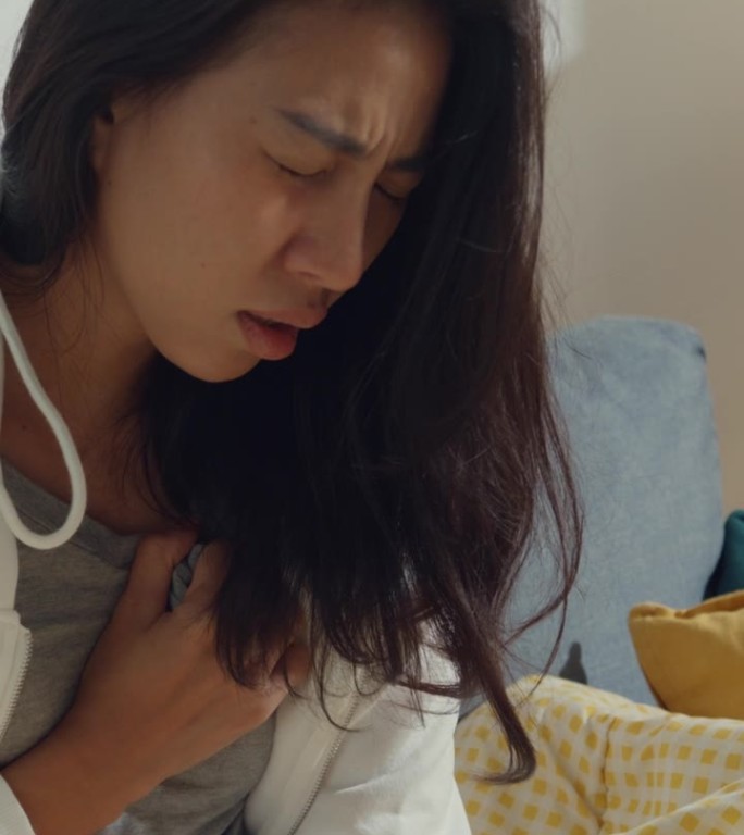 绝望的年轻亚洲女性坐在家中客厅的沙发上，患有癌症。医疗保健概念。