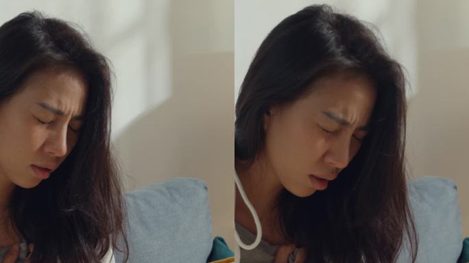 绝望的年轻亚洲女性坐在家中客厅的沙发上，患有癌症。医疗保健概念。