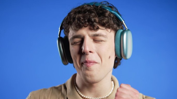 积极的卷发男人听着音乐，戴着现代耳机享受舞蹈