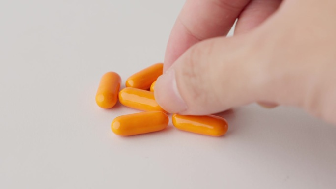 一只手的手指举起了一个橙色的胶囊