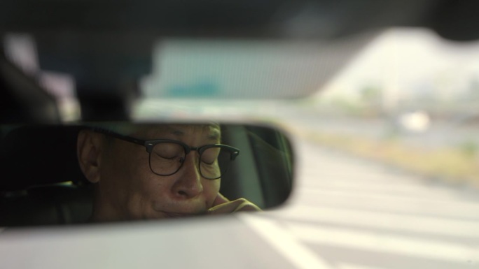 后视镜里的年轻老司机昏昏欲睡。爷爷打了个哈欠，快要睡着了。长时间开车，睡眠不足。老龄化社会的概念。