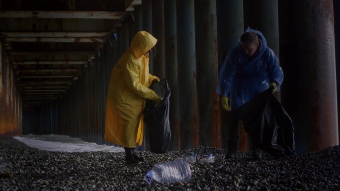 志愿者清理海滩上的垃圾。穿着黄色雨衣的一男一女捡起塑料瓶