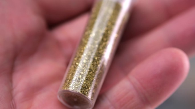 一个详细的微距镜头显示，一个男人的手转动着一个装满闪闪发光的小瓶子，慢慢地分析这种物质。