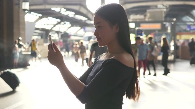 年轻微笑的亚洲女子在火车站用平板电脑上网